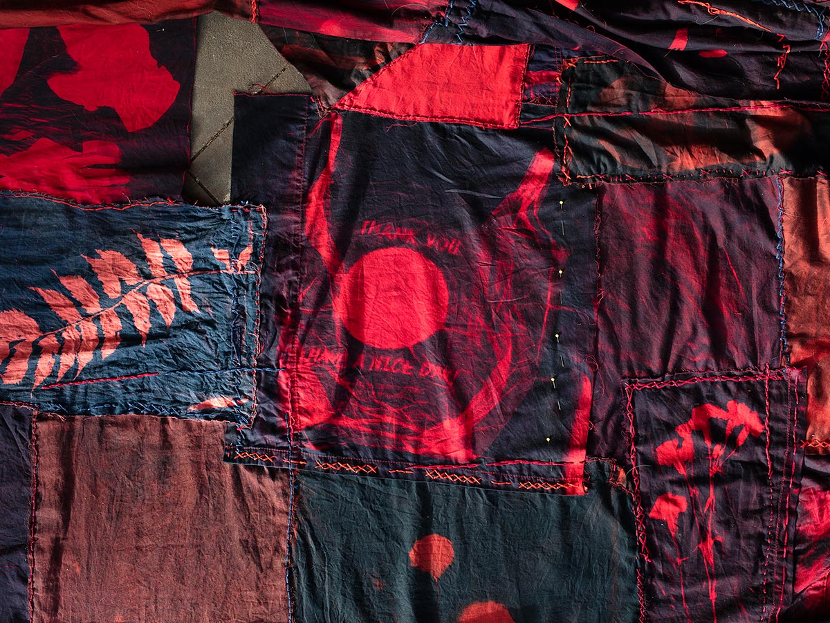 A variety of fabric cyanotypes showing the outline of plants overlaid with red and stitched together.